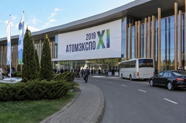 Современный выставочный комплекс с надписью «2019 АТОМЭКСПО XI», флагами и транспортом у входа.