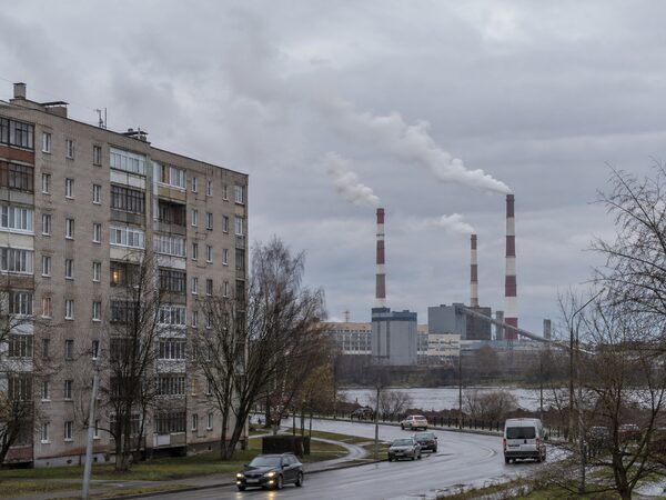 Жилое здание и дорога на переднем плане, промышленные трубы с белыми выбросами вдали.
