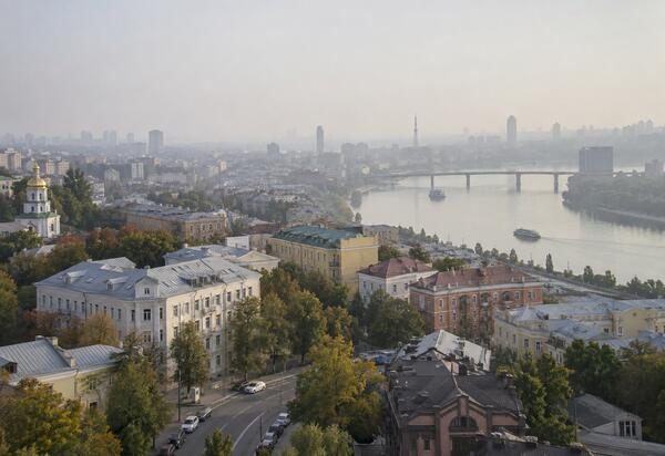 Панорама городской застройки, реки и моста, видимых сквозь плотную атмосферную дымку.